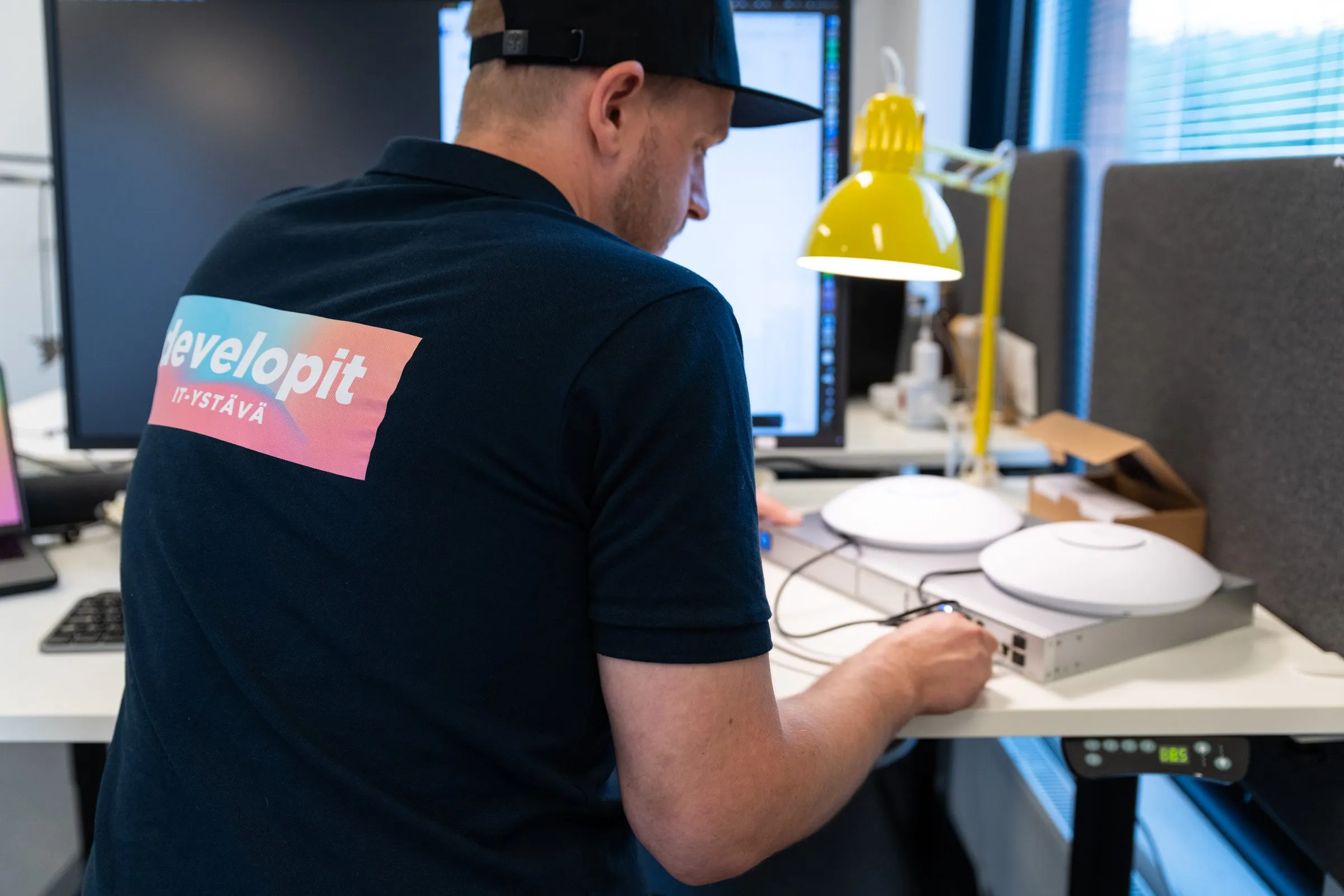 Developitin asentaja kytkee UniFi-tukiasemia verkkokytkimeen työpöydän ääressä.